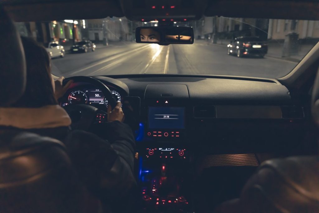Driver navigating city traffic at night, illuminated dashboard in view