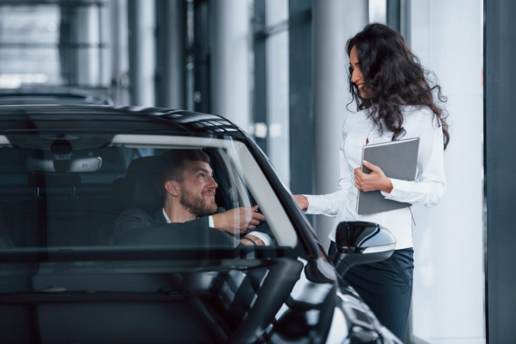 Salesperson advising a customer beside a car in a modern showroom